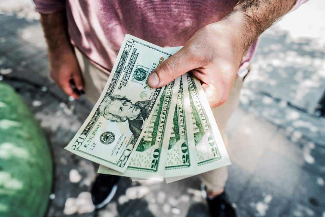 person in red shirt holding four twenty-dollar bills