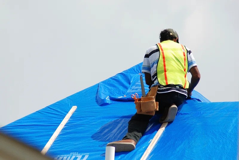 a worker installing an emergency tarp on the roof of a home